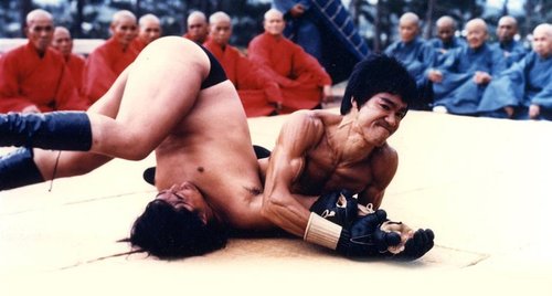 Bruce actually applies a sloppy, early modified armbar on poor Sammo Hung! With the first set of MMA gloves ever made we might add. Holy shit!